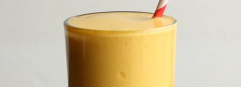 Tall yellow candle with a lit red and white striped wick against a white background