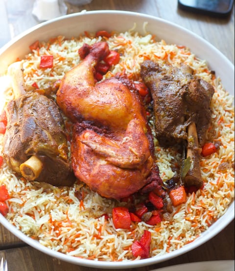 Whole roasted chicken on bed of yellow and white rice with red peppers in white bowl