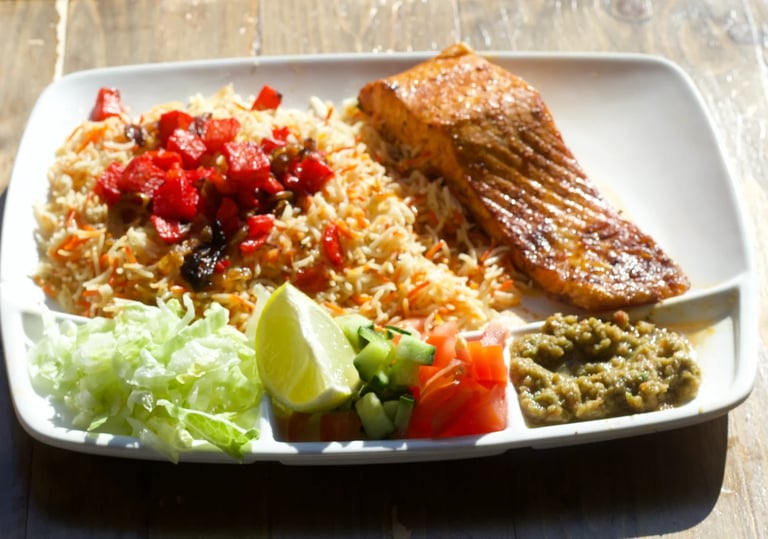 Plated meal with grilled chicken, fried rice topped with red peppers, fresh vegetables, lime wedge, and sauce