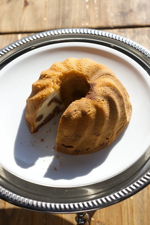 Cinnamon sugar-dusted bundt cake with a slice removed, displayed on a white plate with decorative silver rim