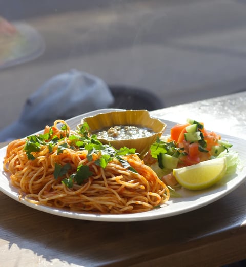 Plate of crispy chow mein noodles with fresh vegetables and lime wedge, served with dipping sauce on white plate