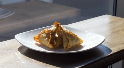 Golden fried samosa on a white plate served on a wooden table in a restaurant setting
